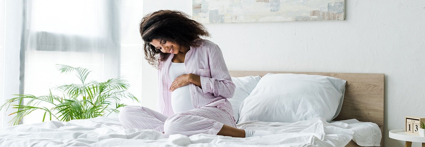 woman sitting on bed cradling belly