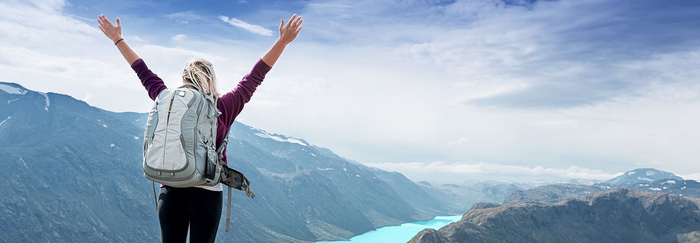 woman stands with arms up overlooking lake