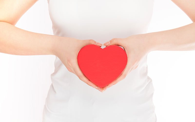 woman holding a red heart in front of her stomach